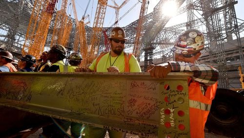 Construction workers sign a steel beam during an event Wednesday to celebrate the near completion of the fixed roof at Mercedes-Benz Stadium. BRANT SANDERLIN/BSANDERLIN@AJC.COM