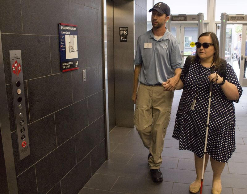 Nick Black, a security officer, walks Katie Hearn to the elevator at SunTrust Park. After Katie lost her vision, she worked hard to relearn many things in her daily life and return to her job with the Atlanta Braves. JENNA EASON / JENNA.EASON@COXINC.COM