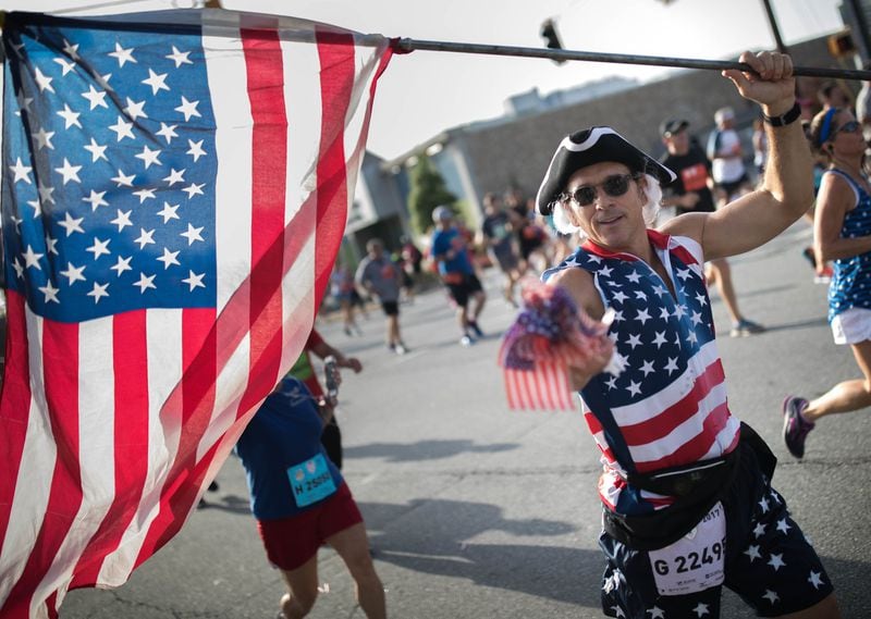 A man runs with an American flag as he makes his way down Peachtree Street during the 48th AJC Peachtree Road Race. (BRANDEN CAMP/SPECIAL)
