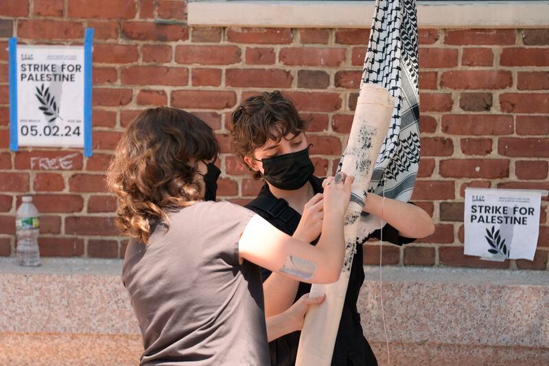 Activists attach a rolled placard to keffiyeh scarves tied together to form a line as they prepare to hoist the banner through an upper floor window to protesters occupying a portion of the building at Rhode Island School of Design, Tuesday, May 7, 2024, in Providence, R.I. The activists are demanding that RISD condemn Israel's war effort in Gaza, and that the school divest from investments that benefit Israel. (AP Photo/Steven Senne)