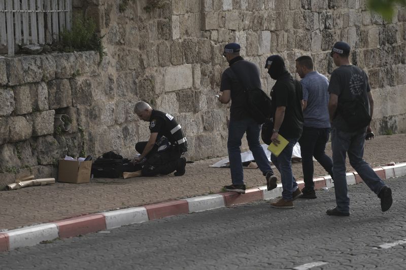 Israeli Police investigate the scene of a stabbing as the body of a suspected attacker lies covered in Ramle, central Israel, Friday, April 26, 2024. The attack, which Israel's rescue services said was carried out by a militant, injured an 18-year-old woman. Paramedics brought her to the hospital in serious condition. Hebrew media reported that the attacker was shot dead shortly after the stabbing. (AP Photo/Mahmoud Illean)