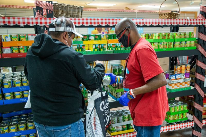 Volunteer Daniel Siler (right) helps clients select canned food at the Solidarity Sandy Springs Food Pantry. PHIL SKINNER FOR THE ATLANTA JOURNAL-CONSTITUTION.
