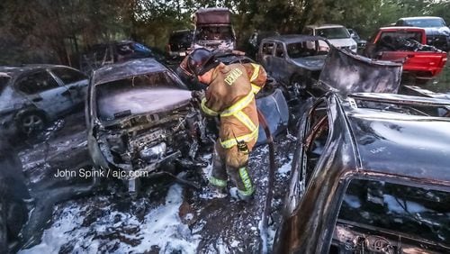 DeKalb County firefighter Joseph Brown works to put out a smoldering vehicle Friday morning, one of at least 12 that burned at a lot attached to an auto body shop north of Lithonia. Two more cars were found burning on Glenwood Road, but officials do not know if the two incidents are connected.