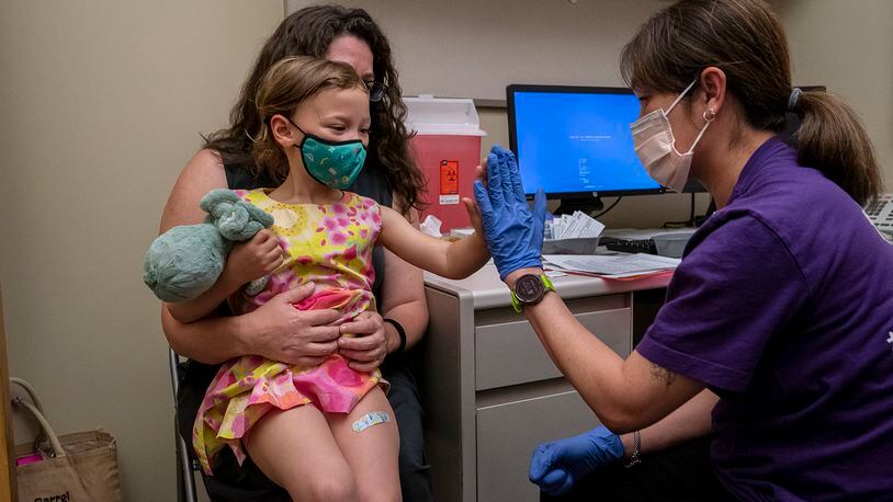 Nora Burlingame, 3, sits on the lap of her mother, Dina Burlingame, and gets a high five from nurse Luann Majeed after receiving her first dose of the Pfizer COVID-19 vaccination at UW Medical Center - Roosevelt on June 21, 2022, in Seattle. (David Ryder/Getty Images/TNS)