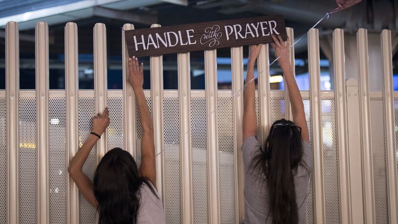 Las Vegas residents (from left) Elisbeth Apcar and Dashenka Giraldo put up a sign reading “Handle With Prayer” at a makeshift memorial at the northern end of the Las Vegas Strip on Oct. 4, 2017, in Las Vegas. On Oct. 1, Stephen Paddock killed 58 people and injured nearly 500 after he opened fire on a large crowd at the Route 91 Harvest country music festival. The massacre is one of the deadliest mass shooting events in U.S. history. DREW ANGERER / GETTY IMAGES