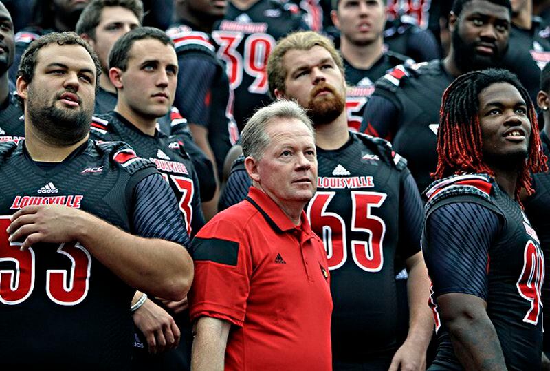 Louisville coach Bobby Petrino, center, and players Jake Smith, left, Brett Nelson (13), David Noltemeyer (65) and Lorenzo Mauldin, right, listen to instructions from the photographer as they prepare for the NCAA college football team photo on media day at Cardinal Stadium in Louisville, Ky., Saturday, Aug. 9, 2014. (AP Photo/Garry Jones) "All these guys? They hate me already." (Garry Jones/AP)