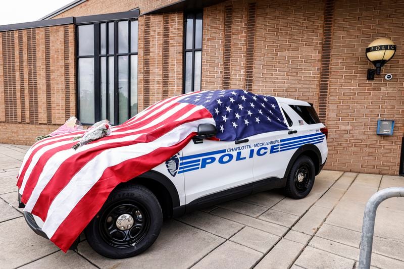 An American flag and flowers cover a Charlotte-Mecklenburg police vehicle at the North Tryon Station in Charlotte, N.C., Tuesday, April 30, 2024 where Charlotte-Mecklenburg Officer Joshua Eyer was stationed. Police in North Carolina say a shootout that killed four law enforcement officers, including Eyer, and wounded four others began as officers approached the home to serve a warrant for a felon wanted for possessing a firearm on April 29. (AP Photo/Nell Redmond)