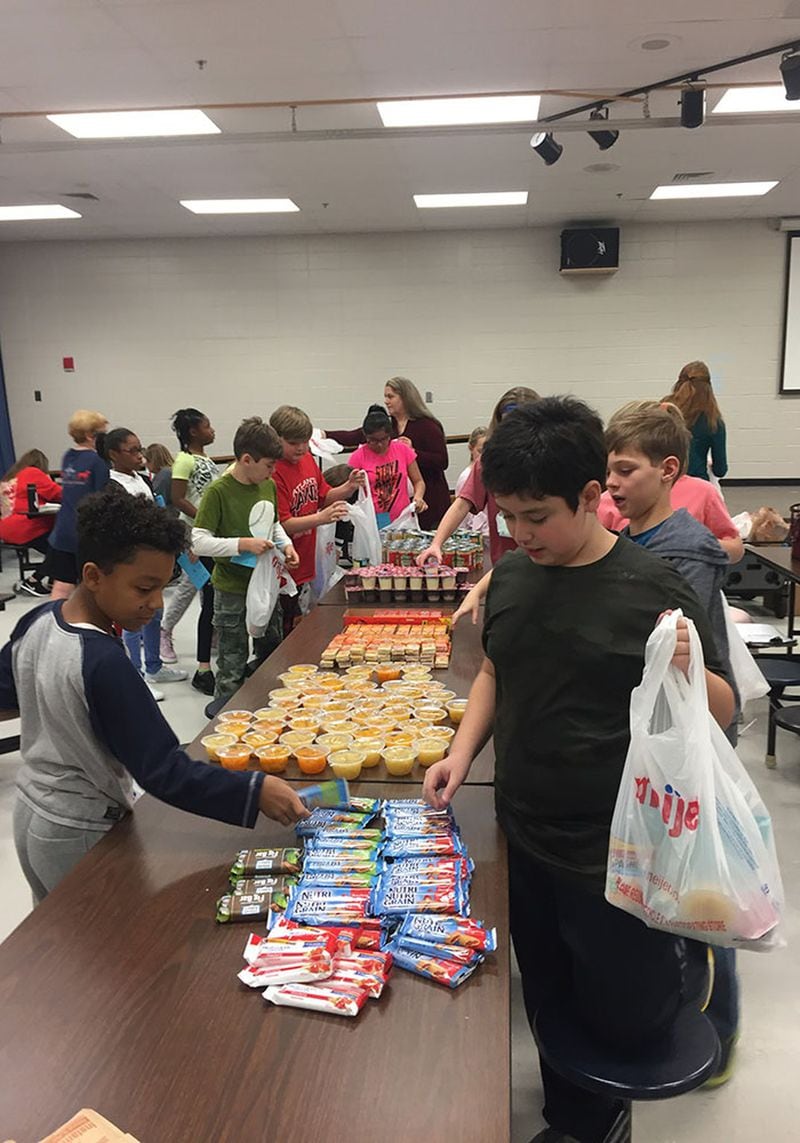 Garrison Mill fifth-grader Nicolas Venegas (at right) packs up snacks for Blessings in a Backpack during a holiday party on Dec. 19. Students prepared food for children who may not have enough to eat during the winter break. CONTRIBUTED BY BLESSINGS IN A BACKPACK