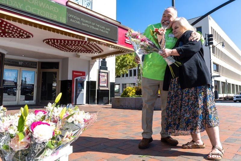 Florist K. Mike Whittle embraces Missy Owen in Marietta Square in Marietta on Wednesday, October 18, 2023, after giving her a free flower bouquet. The event was part of the Society of American Florists' “Petal it Forward” goodwill initiative. (Arvin Temkar / arvin.temkar@ajc.com)