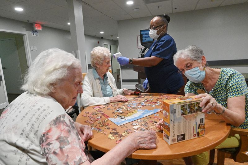 July 14, 2021 Smyrna - Joan Telotte gets a temperature check from Anna Williams (standing) as Kathryn Trice (right), activities director, helps Shirley McGahan (left) with Jigsaw puzzle at Woodland Ridge Assisted Living on Wednesday, July 14, 2021. (Hyosub Shin / Hyosub.Shin@ajc.com)