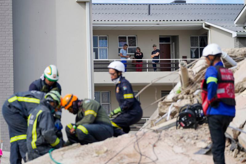 Residents watch rescue workers search the site of a building collapse in George, South Africa, Wednesday, May 8, 2024. Rescue teams are searching for dozens of construction workers missing after a multi-story apartment complex collapsed in the coastal city have brought out more survivors as the operation entered a second night of desperate work to find anyone alive in the mangled wreckage. (AP Photo/Jerome Delay)