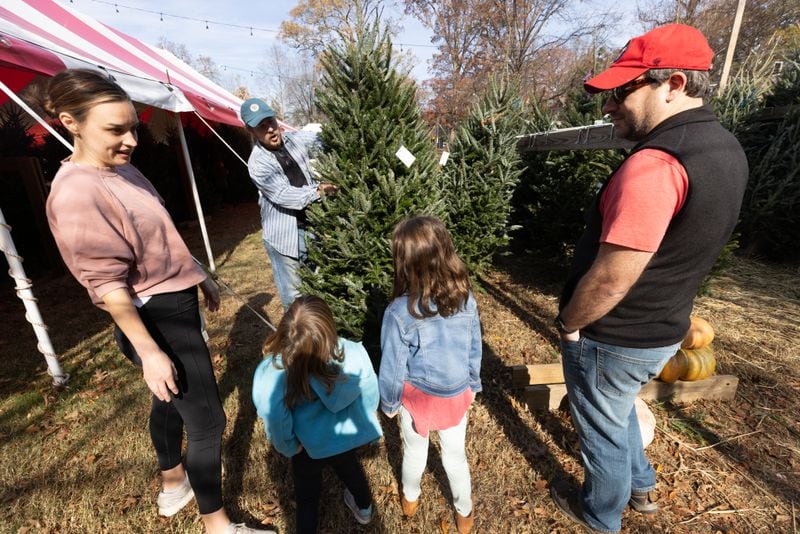 Owner Calder Johnson shows a tree to the Sheidler family at his Trees For Tuition lot in Virginia-Highland on Saturday, Nov. 25, 2023.  (Steve Schaefer/steve.schaefer@ajc.com)