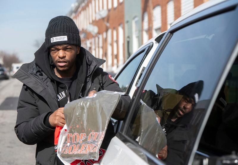 Antonio Moore, 24, of Baltimore, hands out designer t-shirts reading "Stop Gun Violence" in his childhood neighborhood in east Baltimore, Monday, Feb. 26, 2024. Moore, is a successful real estate investor and entrepreneur who founded a consulting company that helps brands and nonprofits connect with urban youth. (AP Photo/Steve Ruark)