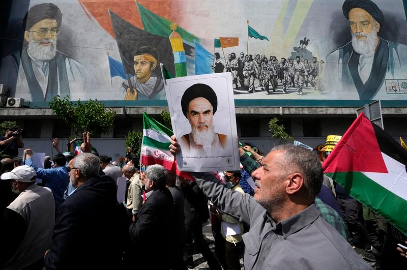 Iranian worshippers walk past a mural showing the late revolutionary founder Ayatollah Khomeini, right, Supreme Leader Ayatollah Ali Khamenei, left, and Basij paramilitary force, as they hold a poster of Ayatollah Khomeini and Iranian and Palestinian flags in an anti-Israeli gathering after their Friday prayer in Tehran, Iran, Friday, April 19, 2024. An apparent Israeli drone attack on Iran saw troops fire air defenses at a major air base and a nuclear site early Friday morning near the central city of Isfahan, an assault coming in retaliation for Tehran's unprecedented drone-and-missile assault on the country. (AP Photo/Vahid Salemi)