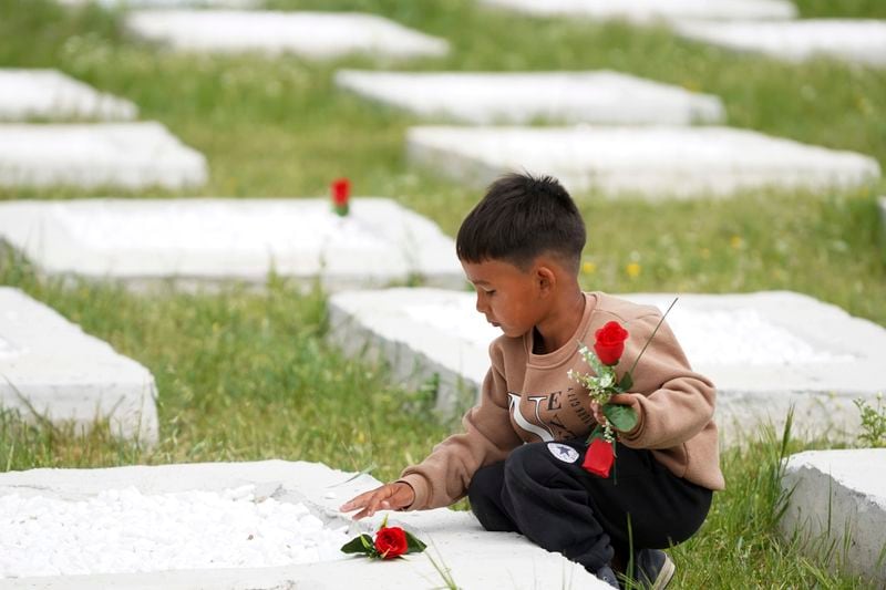 A boy lays flowers on a grave at the cemetery in Kato Tritos village on the northeastern Aegean Sea island of Lesbos, Greece, on Wednesday, April 17, 2024. After years of neglect, a primitive burial ground for refugees who died trying to reach Greece's island of Lesbos has been cleaned up and redesigned to provide a dignified resting place for the dead. (AP Photo/Panagiotis Balaskas)