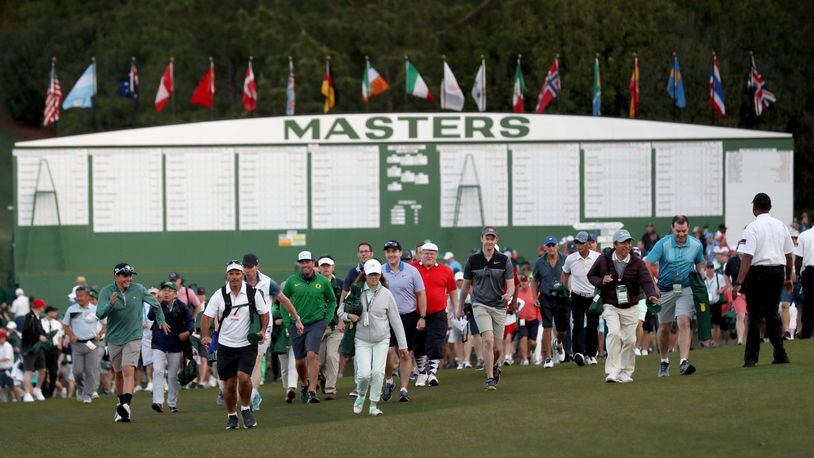 Patrons enter the grounds and walk toward the first tee crossing in front of the Masters scoreboard before the start of the 2019 tournament Thursday, April 11, 2019, at Augusta National Golf Club in Augusta.