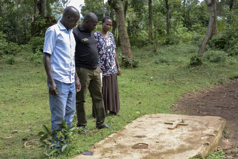 Humphrey Kizito, centre, with his brother and sister in law, stand by their parents gravesite at their home in Siaya, Kenya Saturday, April. 13, 2024. Even after parts of Kenya participated in an important pilot of the world's first malaria vaccine, with a reported drop in deaths for children under 5, the disease is still a significant public health challenge. Kenya's health ministry hasn't said when the vaccine will be widely available. (AP Photo/Brian Ongoro)