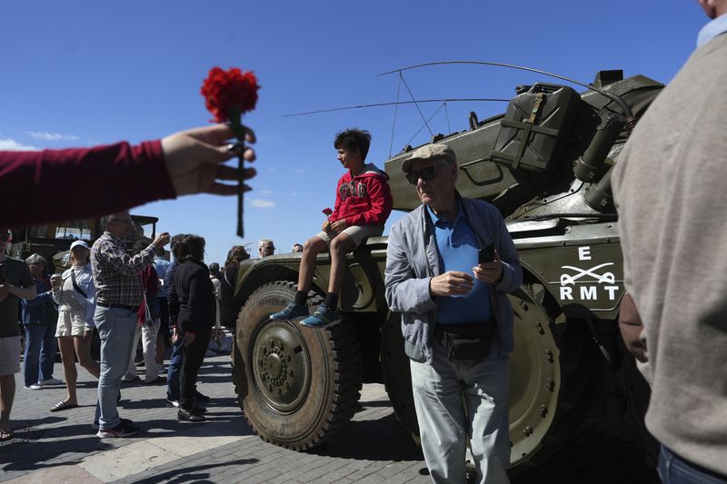 A child holding a red carnation sits on a military vehicle that took part in the 1974 Carnation revolution, on display at Lisbon's Comercio square, Thursday, April 25, 2024, during celebrations of the fiftieth anniversary of the military coup. The April 25, 1974 revolution carried out by the army restored democracy in Portugal after 48 years of a fascist dictatorship. (AP Photo/Ana Brigida)