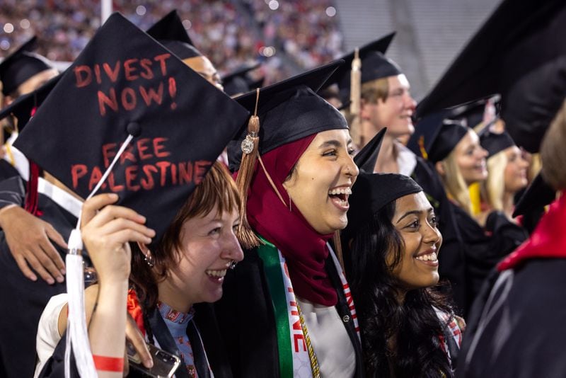 A graduate holds a graduation cap with a pro-Palestinian message in Sanford Stadium while a singer sings Georgia on My Mind during the University of Georgia spring commencement in Athens on Friday, May 10, 2024. (Arvin Temkar / AJC)