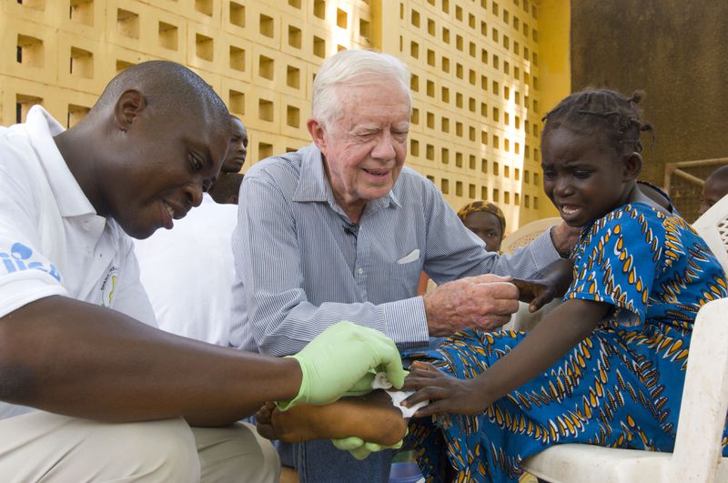 Jimmy Carter consoles a young patient having a Guinea worm removed from her body in Savelugu, Ghana, in February 2007. The Carter Center led the international campaign to eradicate Guinea worm disease. (The Carter Center)