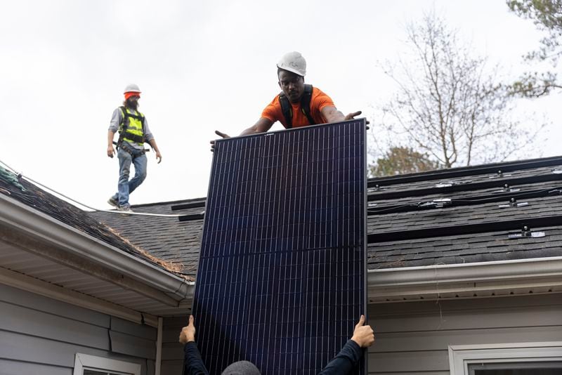 Joe McClain, left, and Mike Harris, right, installers for Creative Solar USA, move solar panels onto the roof of a home in Ball Ground, Georgia on December 17th, 2021. 