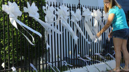 A woman covers the fence of the Emanuel AME Church with white ribbons and flowers in June 2015 in Charleston. A lone white killer struck a Wednesday night prayer service at the church killing 9 including the pastor. (Curtis Compton / AJC file)