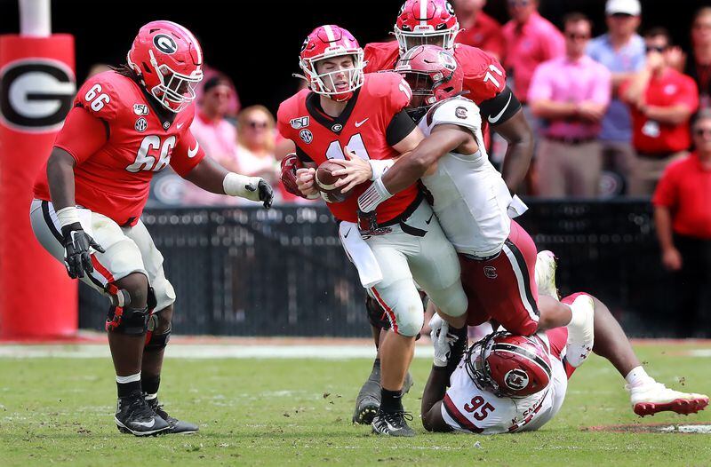 Georgia quarterback Jake Fromm is sacked by South Carolina defenders Kobe Smith (bottom) and D.J. Wonnum (top) during the third quarter in a NCAA college football game on Saturday, October, 12, 2019, in Athens.    Curtis Compton/ccompton@ajc.com