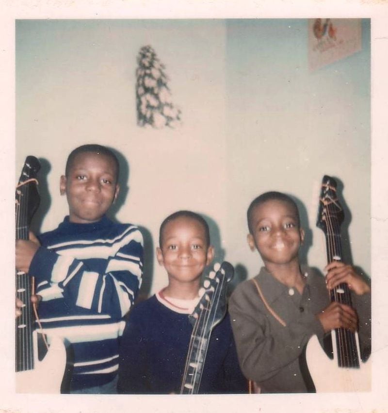 Vernon Washington (left) and Rodney Washington (right) flank youngest brother Wayne Washington as they hold guitars they received as a Christmas gifts. (Washington family photo)