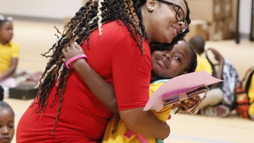 Second-grade teacher Anesha Williams gives Malae Tucker a hug as they gather in the gym on the first day of school at Tuskegee Airmen Global Academy. Bob Andres / robert.andres@ajc.com