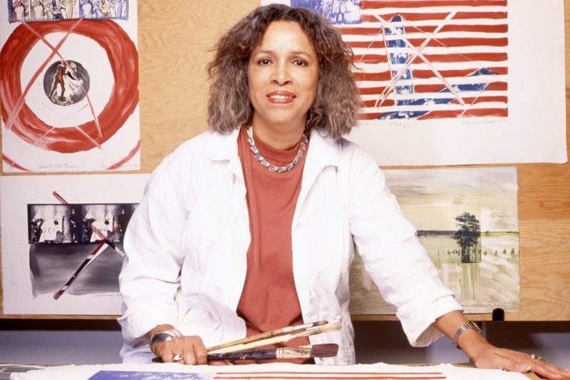 The new Georgia Museum retrospective: "Emma Amos: Color Odyssey," opens on Jan. 30, in Athens. Amos, born in Atlanta, used her career to challenge ideas around race, sex, and class. Behind her is a version of her piece "About Whiteness." Amos died in 2020 from complications due to Alzheimer's disease.