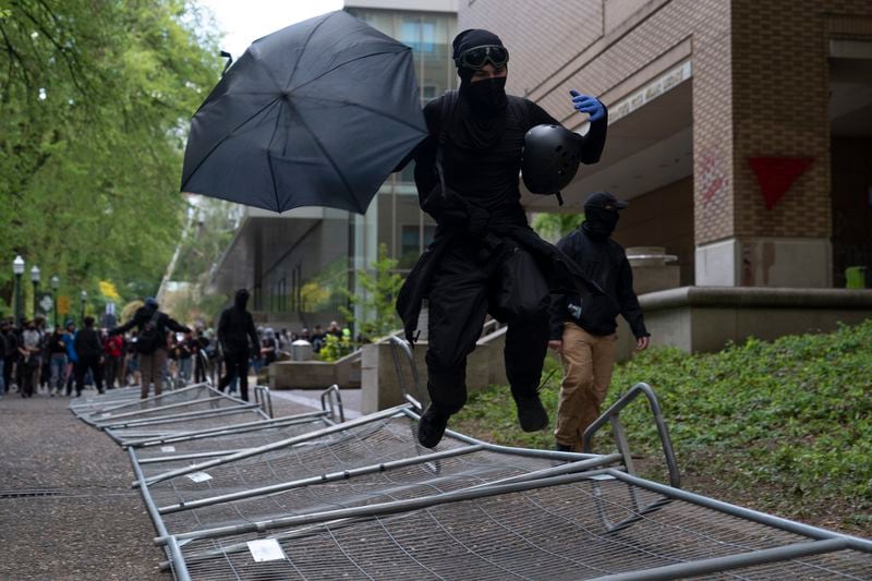 A pro-Palestinian protester jumps on fencing outside a library on the Portland State University campus on Thursday, May 2, 2024, in Portland, Ore. The fencing was placed by police after they cleared out the library that had been occupied by protesters since Monday. Officers said they made 22 arrests Thursday. (AP Photo/Jenny Kane)