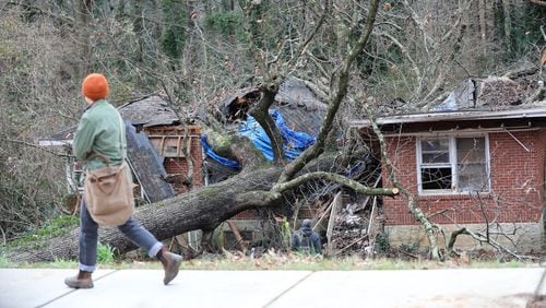 A person walks in front of the house on Glenwood Road where a tree fell in DeKalb County, killing a 5-year-old boy. (Credit: Miguel Martinez for The Atlanta Journal-Constitution)