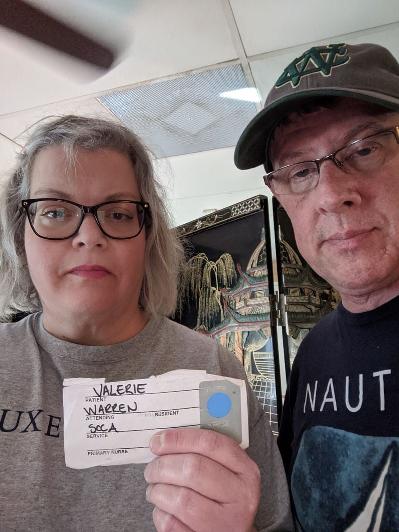 Rachel Grimes and her husband, Greg, for whom the coronavirus poses increased health risks. She is holding the hospital tag of a patient she met during her husband’s bone marrow transplant in Seattle 20 years ago. The woman, Valerie, died. 