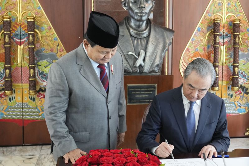 Indonesian President-elect and current Defense Minister Prabowo Subianto, left, stands next to Chinese Foreign Minister Wang Yi as Wang signs a guest book in Jakarta, Indonesia, Thursday, April 18, 2024. (AP Photo/Achmad Ibrahim/Pool)