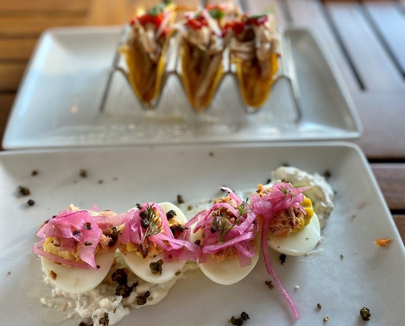 The deviled eggs at Seed Kitchen & Bar are topped like bagels, with smoked salmon, capers and pickled red onion. A trio of smoked chicken tacos sits in the background. (Wendell Brock for The Atlanta Journal-Constitution)