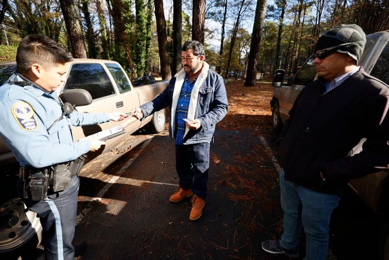 Sr. Officer Daniel Arrata talks in Spanish with Gwinnett residents Gilberto Perez, center, and Ricardo Salmeron; Officer Arrata helped investigate a bin number from a vehicle Perez tried to sell to Salmeron.
 Miguel Martinez / miguel.martinezjimenez@ajc.com
