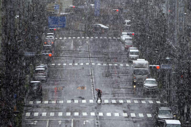A woman walks in falling snow Saturday in Tokyo. Tokyo Gov. Yuriko Koike has repeatedly asked the city’s 13 million residents to stay home this weekend, saying the capital is on the brink of an explosion in virus infections.