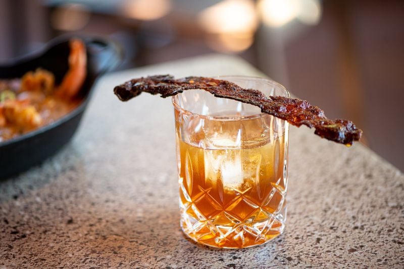 Smoked Maple Bacon Old Fashioned with  housemade bacon-washed Tincup Mountain Whisky, cedar smoke, Montenegro Amaro liqueur, bitters, maple syrup, and bacon candy. Photo credit- Mia Yakel.