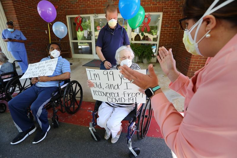 Westbury Medical Care & Rehab administrator Jennifer Vasil applauds then 99-year-old COVID-19 survivor Irma Gooden, who has since turned 100, and Johnny Simmons, 65, while preparing to hold a celebration for the recovery of some of the facility residents in May. CURTIS COMPTON / CCOMPTON@AJC.COM