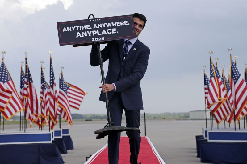 A campaign worker carries out a podium that indicates former President Donald Trump will debate President Joe Biden anytime, anywhere or anyplace, before Trump speaks at a rally in Wilmington, N.C., Saturday, April 20, 2024. (AP Photo/Chris Seward)