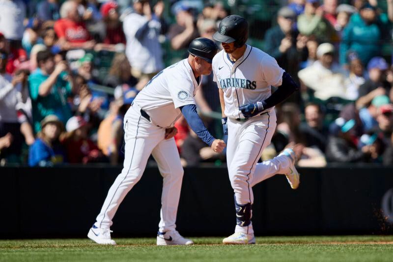 Seattle Mariners designated hitter Mitch Garver is congratulated by third base coach Manny Acta as he rounds the bases after hitting a solo home run off a pitch fromCincinnati Reds pitcher Andrew Abbott during the sixth inning of a baseball game, Wednesday, April 17, 2024, in Seattle. (AP Photo/John Froschauer)