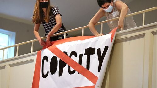 080521 Atlanta: Local activists Kelsea (left) and Nora (right), who go by first names only, hang a "Stop Cop City" banner from the balcony of the Neighborhood Church during a town hall meeting to gather public input in opposition to the plans for a new police and fire training facility in DeKalb County on Thursday, August 5, 2021, in Atlanta.   “Curtis Compton / Curtis.Compton@ajc.com”