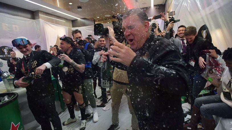 Atlanta United head coach Gerardo Martino gets soaked with beers as players celebrate in their locker room after Atlanta United beat the Portland Timbers Saturday, Dec. 8, 2018, for the MLS Cup championship.