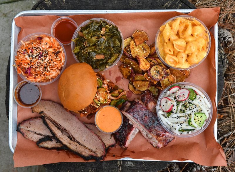 The sampler platter at Heirloom Market BBQ includes (clockwise from top left) kimchi slaw, collard greens, Korean sweet potatoes, mac and cheese, cucumber radish salad, gochujang ribs, spicy Korean pork sandwich and miso brisket.(CHRIS HUNT FOR THE ATLANTA JOURNAL-CONSTITUTION)