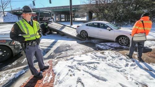 January 17, 2018 Atlanta: GSP trooper S. Stone (left) waits on a Mazda 6 to be towed from the scene after James May (right) skidded on the ice on Joseph E. Lowery Blvd. striking a concrete sewer on the I-20 entrance ramp and breaking his axle. No one was hurt. JOHN SPINK/JSPINK@AJC.COM