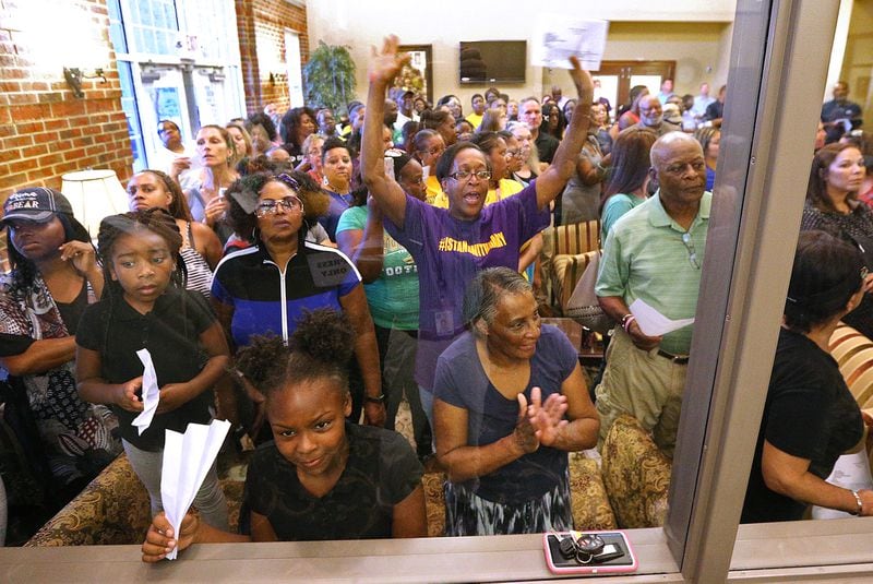 An overflow crowd reacts from the lobby outside the glass window at the back of the room during the Buford Board of Education meeting at the Central Office board room on Monday, August 27, 2018, in Buford. It is the first meeting since Superintendent Geye Hamby resigned amid allegations he used racial slurs to refer to black temporary construction workers and threatened violence against them.