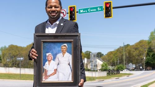 Deonté Smith stands under a street sign dedicated to his great grandmother and great-great grandmother while holding a painting of them in McDonough. (Atlanta Journal-Constitution/Jason Allen)