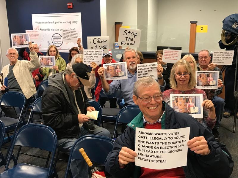 A group believed to be organized by Debbie Dooley holds up signs as Gwinnett elections staff counts provisional ballots prior to election board meeting.