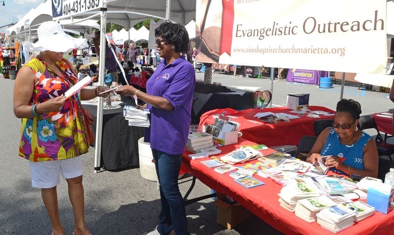 Barbara Massey of Zion Baptist Church of Marietta distributes a copy of Our Daily Bread to passer-by Sabrina Wallace (hat) of Marietta at the 11th Annual Juneteenth Cultural Festival. (PHOTO M. CHRIS HUNT)