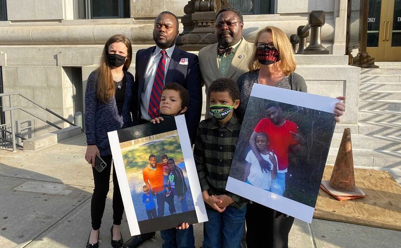Family members of the late Antonio May and their lawyers stand on the steps of the Fulton County Courthouse in Atlanta on Nov. 16, 2021, after the indictment of six deputy sheriffs. In the foreground are two of May's three sons holding family photos. Top row from left, Shonna Rickerson, the boys' mother; attorneys Michael Harper and Teddy Reese; and April Myrick, legal guardian of both boys.